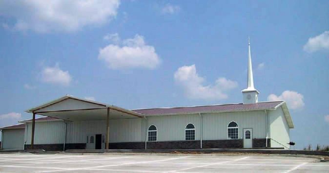 A church with a steeple and a parking lot in front of it.